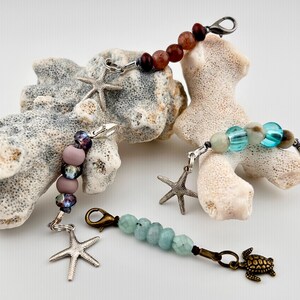May include: Four beaded keychain charms with starfish and turtle accents. The charms feature various colors of beads, including red, purple, and turquoise. The charms are attached to silver and bronze-colored clasps.