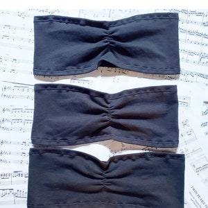 Puede incluir: Tres tops de tubo negros hechos de un tejido suave y elástico. Los tops de tubo están colocados sobre una hoja de música.