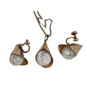 May include: A gold-toned jewelry set featuring a pendant necklace and clip-on earrings. Each piece has a gold-colored, petal-shaped frame holding a white, iridescent, spherical stone. The set is displayed against a white background.