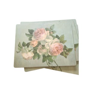 Könnte beinhalten: Ein Set rechteckiger Platzsets mit einem weichen, blassgrünen Hintergrund und einer zentralen Illustration blühender rosa und weißer Rosen, umgeben von grünen Blättern. Das Design wiederholt sich auf den gestapelten Artikeln und zeigt florale Details.