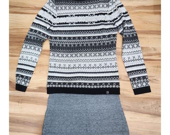 May include: Black and white patterned sweater with a grey skirt. The sweater has a crew neck and long sleeves. The skirt is a-line and hits above the knee.