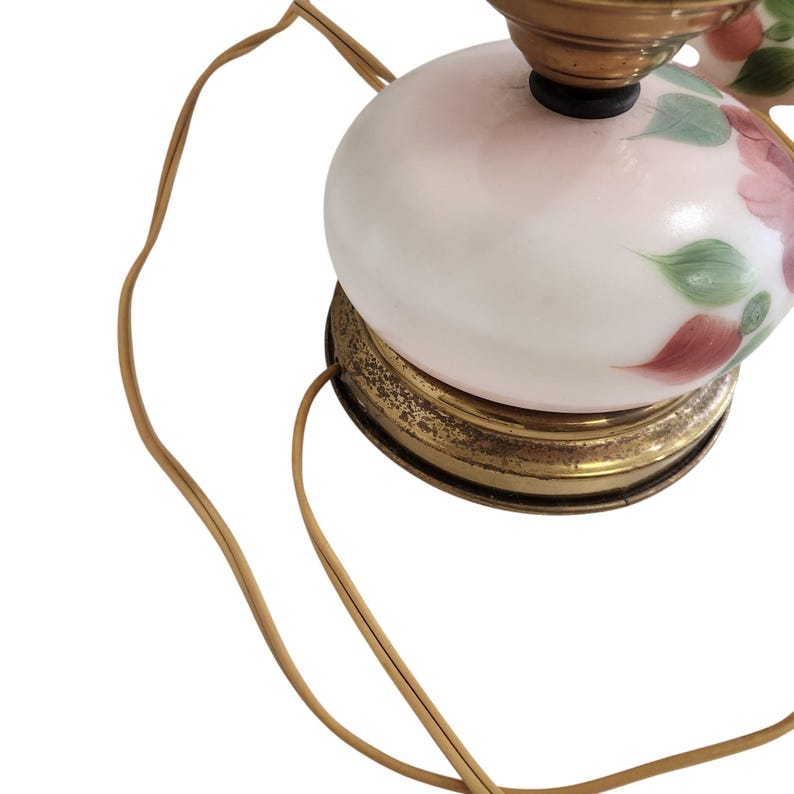 May include: A white glass lamp base with a floral design in shades of pink, green, and brown. The lamp base has a gold metal rim and a gold metal cord.