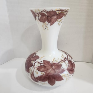 Puede incluir: Jarrón de cristal blanco con base bulbosa y parte superior acampanada. El jarrón está decorado con hojas granates pintadas a mano y detalles dorados. Una pieza decorativa para la decoración del hogar.