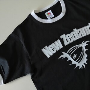 May include: Black t-shirt with a white graphic of a rugby ball and the text "New Zealand".