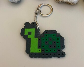 May include: A green and black pixelated snail keychain with a silver key ring.