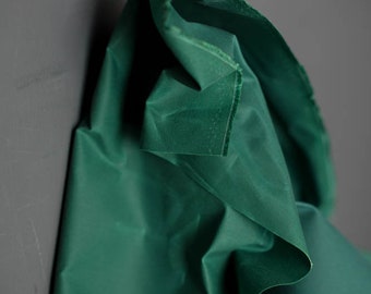 May include: A deep green fabric with a smooth, silky texture. The fabric is folded and draped, showcasing its soft, flowing quality.