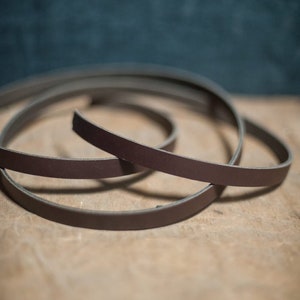 May include: A close-up of a brown leather strap coiled on a wooden surface.
