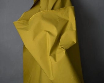 May include: A close-up of a mustard yellow fabric with a smooth, silky texture. The fabric is folded and draped, showcasing its drape and flow.