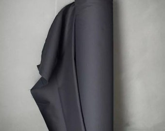 May include: A roll of dark navy blue fabric. The fabric is tightly wound around a cardboard tube, with a portion of the fabric unrolled, revealing its smooth texture. A small tag is attached to the tube.