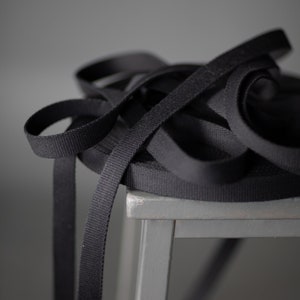 May include: A close-up of a pile of black webbing on a gray wooden stool. The webbing is thick and has a woven texture.