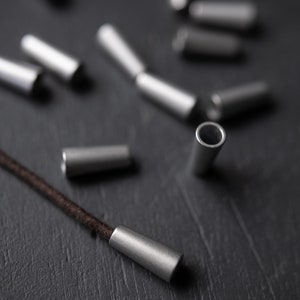 May include: A close-up of silver metal cord ends on a black surface. A brown cord is threaded through one of the cord ends.