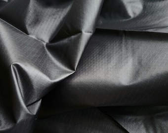 May include: Black fabric with a subtle sheen and a textured weave. The fabric is folded and draped on a wooden surface.
