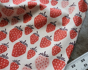 May include: A white fabric with a repeating pattern of red and pink strawberries. The fabric is folded and a ruler is visible in the bottom right corner.