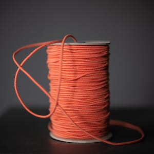 May include: A spool of orange elastic cord, wound tightly and ready to be used for crafting projects.