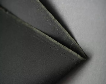 May include: Close-up of a black fabric with a textured surface and a stitched edge.