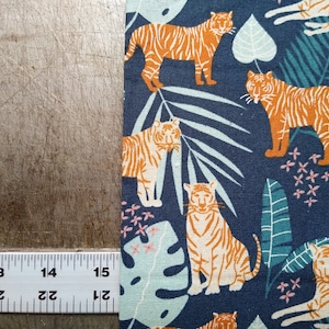 May include: A navy blue fabric with a repeating pattern of orange tigers and green tropical leaves. The tigers are depicted in a stylized, cartoon-like manner.