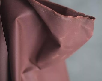May include: Close-up of a folded piece of fabric in a muted mauve color. The edges of the fabric are slightly frayed, adding texture. The background is a soft, blurred gray.