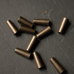 May include: A group of ten small, gold-colored metal caps scattered on a dark gray surface.