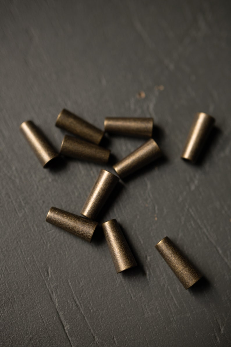 May include: A group of ten small, gold-colored metal caps scattered on a dark gray surface.