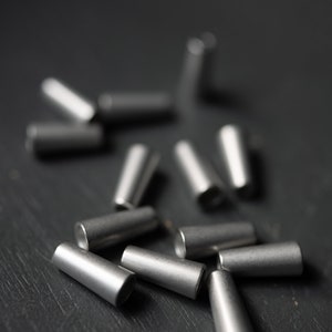 May include: A close-up of a group of silver metal cable end caps scattered on a dark gray surface.