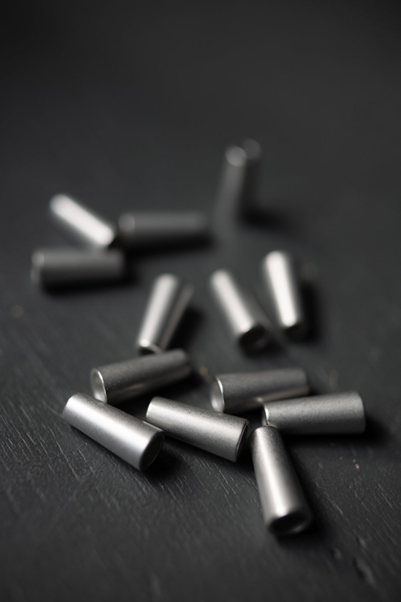 May include: A close-up of a group of silver metal cable end caps scattered on a dark gray surface.