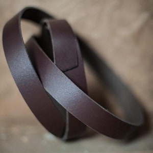 May include: Two pieces of dark brown leather strap, one wrapped around the other, creating a circular shape.
