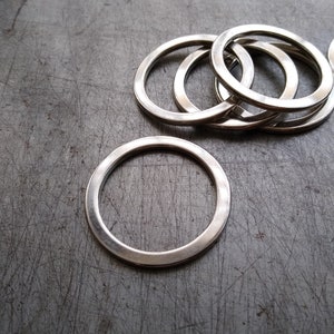May include: A stack of silver metal rings, with one ring separated from the stack and lying on a gray textured surface.