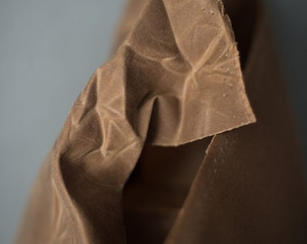 May include: Close-up of a brown fabric with a textured surface. The fabric is folded and creased, showing the natural texture of the material.