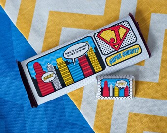 May include: A white chocolate bar wrapped in a comic book style wrapper with a red, yellow, and blue cityscape and the text "THIS IS A JOB FOR SUPER JEFFREY!" and "SUPER SWEET!"