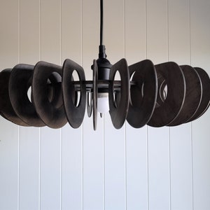 Puede incluir: Una lámpara de techo de metal negro con un diseño circular. La lámpara tiene múltiples anillos superpuestos, creando un aspecto único y moderno.