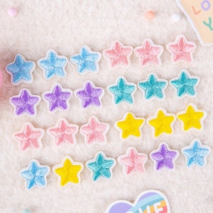 Può includere: Una collezione di 24 toppe ricamate a forma di stella di diversi colori, da applicare con il ferro da stiro. Le toppe sono di vari colori, tra cui rosa, blu, viola, giallo e turchese.