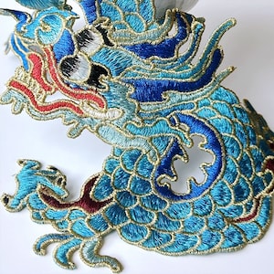 Peut inclure: Une applique brodée de dragon bleu et or avec des accents rouges. Le dragon est détaillé avec des écailles et a une expression féroce.