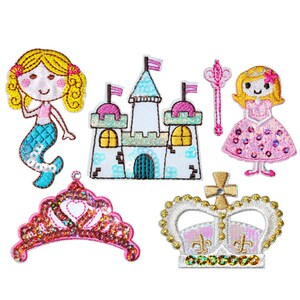 Może przedstawiać: Zestaw sześciu naszywek do prasowania przedstawiających księżniczkę, syrenkę, zamek, koronę, tiarę i różdżkę. Naszywki są ozdobione cekinami i haftem.