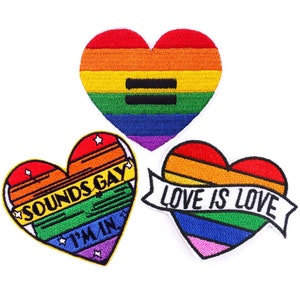 May include: Three embroidered iron-on patches in the shape of hearts. The first patch is a rainbow heart with a black equals sign. The second patch is a rainbow heart with the text "SOUNDS GAY I'M IN". The third patch is a rainbow heart with the text "LOVE IS LOVE" on a white banner.