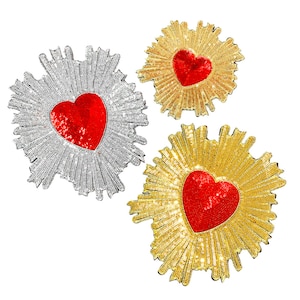 May include: Three heart-shaped patches with a sunburst design. The patches are made of sequins and have a red heart in the center. The patches are silver, gold, and gold.