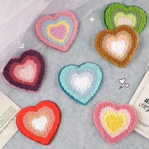Può includere: Sette toppe di feltro a forma di cuore di diversi colori con un design a strati. Ogni toppa ha una diversa combinazione di colori, tra cui rosa, blu, verde, giallo e rosso.