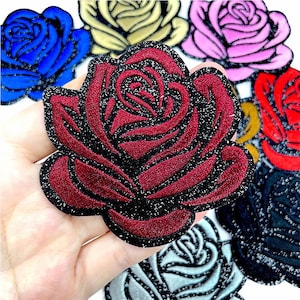 以下が含まれることがあります： 赤、青、黄色、ピンクなど、様々な色のバラの刺繍ワッペン。赤いバラは黒い縁取りとキラキラしたアクセントが特徴です。衣類やクラフトプロジェクトに適しています。
