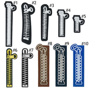 Peut inclure: Une collection de dix écussons de fermeture éclair brodés de différentes couleurs et tailles. Les écussons comprennent des fermetures éclair blanches, noires, dorées, marron, bleu marine et bleues. Chaque écusson présente un motif détaillé d'une fermeture éclair.