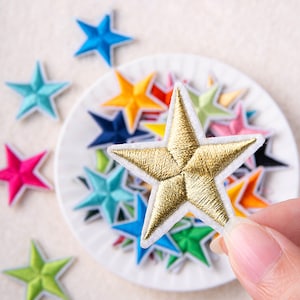 Pode incluir: Uma coleção de patches bordados em forma de estrela de várias cores, incluindo um patch de estrela dourada com contorno branco.