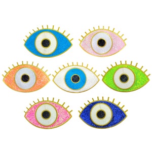 May include: Set of six colourful evil eye charms with gold trim. Each charm features a white eye with a black pupil and a glittery background.
