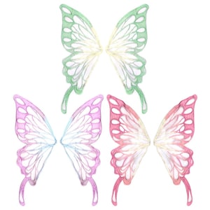 Può includere: Tre paia di ali di fata in diversi colori. Le ali sono realizzate in un materiale delicato e traslucido e hanno un design delicato e intricato. Le ali sono in tonalità di verde, rosa e blu.