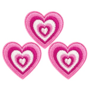 Pode incluir: Três patches bordados em forma de coração rosa e branco. Cada coração tem um desenho concêntrico de círculos rosa e brancos.