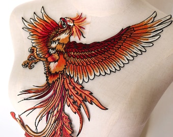 Op de afbeelding: Een grote geborduurde patch met een rode en oranje feniks met zwarte contouren. De feniks is in vlucht met zijn vleugels wijd gespreid en zijn staartveren die achter hem stromen.
