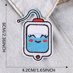 May include: A blue and white embroidered iron-on patch of a cartoon IV bag with a smiling face, red cheeks, and eyelashes. The IV bag has a red top and a white straw. The patch is 4.2 cm by 6 cm.
