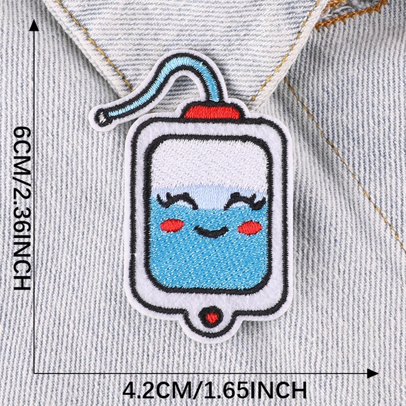 May include: A blue and white embroidered iron-on patch of a cartoon IV bag with a smiling face, red cheeks, and eyelashes. The IV bag has a red top and a white straw. The patch is 4.2 cm by 6 cm.