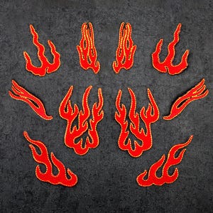 Könnte beinhalten: Eine Sammlung roter Flammenaufnäher mit goldfarbenen Rändern. Die Aufnäher sind in verschiedenen Formen und Größen gehalten und stellen stilisierte Flammen dar. Diese gestickten Aufnäher eignen sich zum Aufnähen auf Kleidung oder Accessoires.