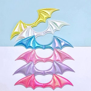 May include: An assortment of iridescent bat wing patches in shades of yellow, white, blue, pink, and purple. The patches have a glossy, metallic appearance and are arranged in a layered design against a light blue and white backdrop.