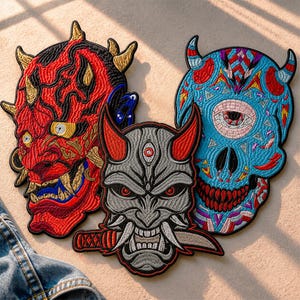 May include: Three embroidered patches featuring detailed designs. One is a red demon face with gold horns, another is a blue skull with an eye, and the third is a gray demon mask with a knife. The patches have black borders.