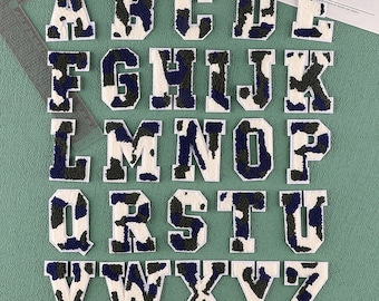 May include: A set of 26 iron-on alphabet letters in a white, black, and blue camouflage pattern. The letters are uppercase and are approximately 2 inches tall.