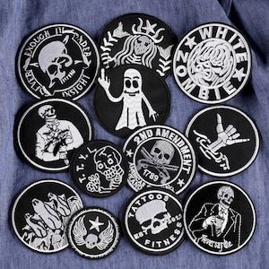 Peut inclure: Un ensemble de 11 patchs brodés thermocollants noirs et blancs représentant différents motifs de crânes, dont un fantôme, un zombie, un squelette tenant une arme à feu et un crâne avec des os croisés. Les patchs sont circulaires et présentent des coutures blanches sur un fond noir.